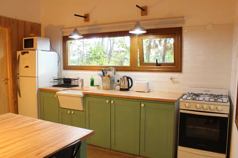Cocina con alacenas verdes y ventana al bosque